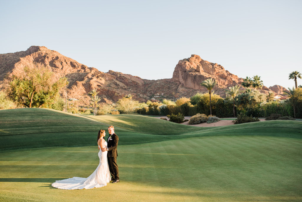 Bride and groom walking at their Mountain Shadows Wedding on golf course with mountains in the back