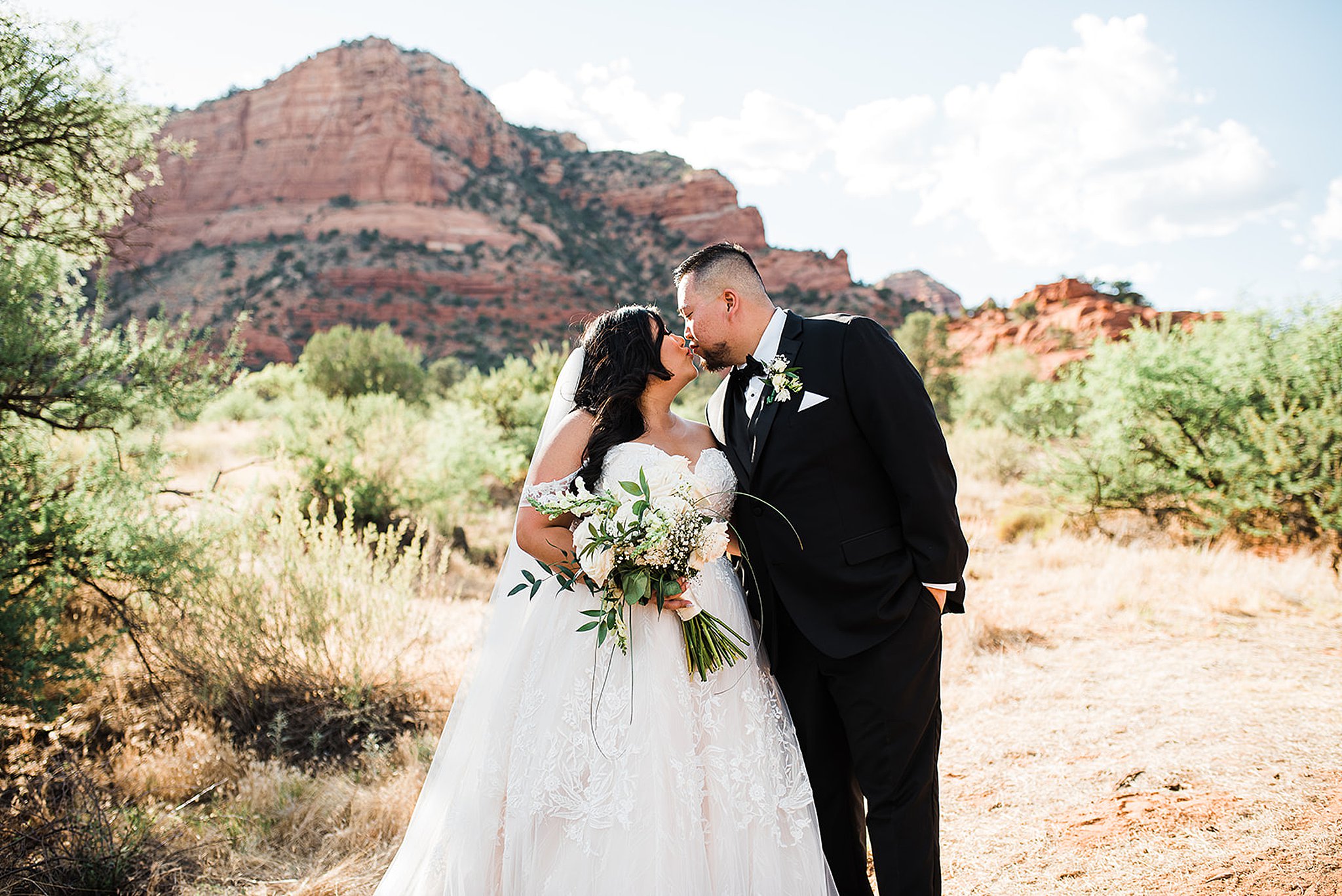 bride and groom sharing a kiss in front of the red rocks at red agave resort
