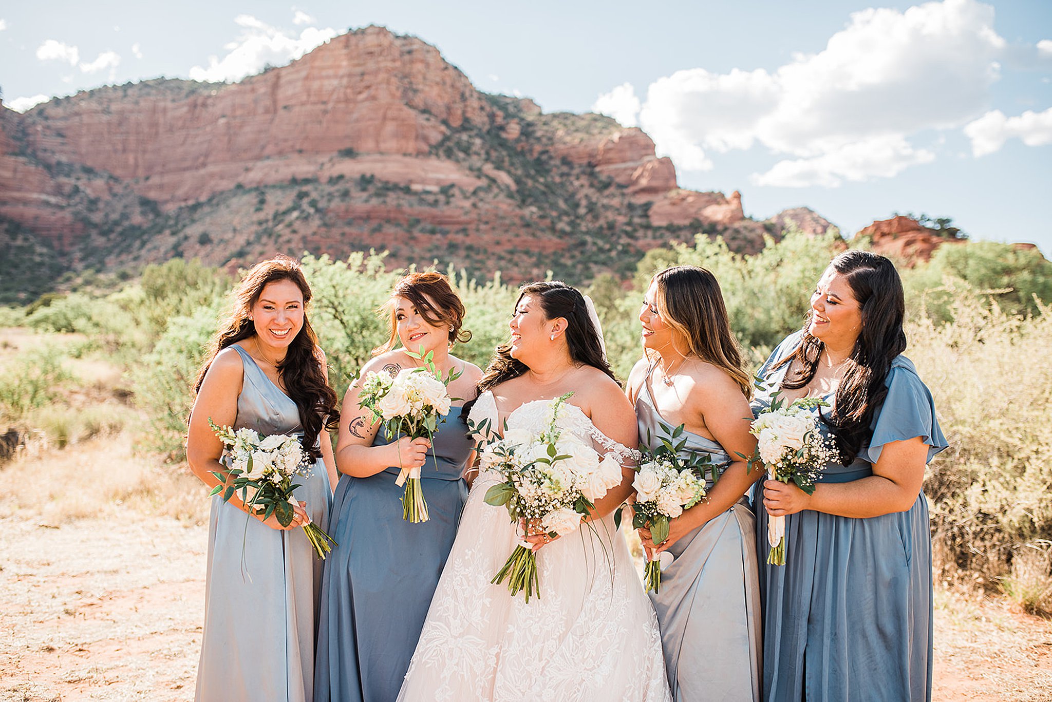 bridal party stands in the desert holding their white bouquets