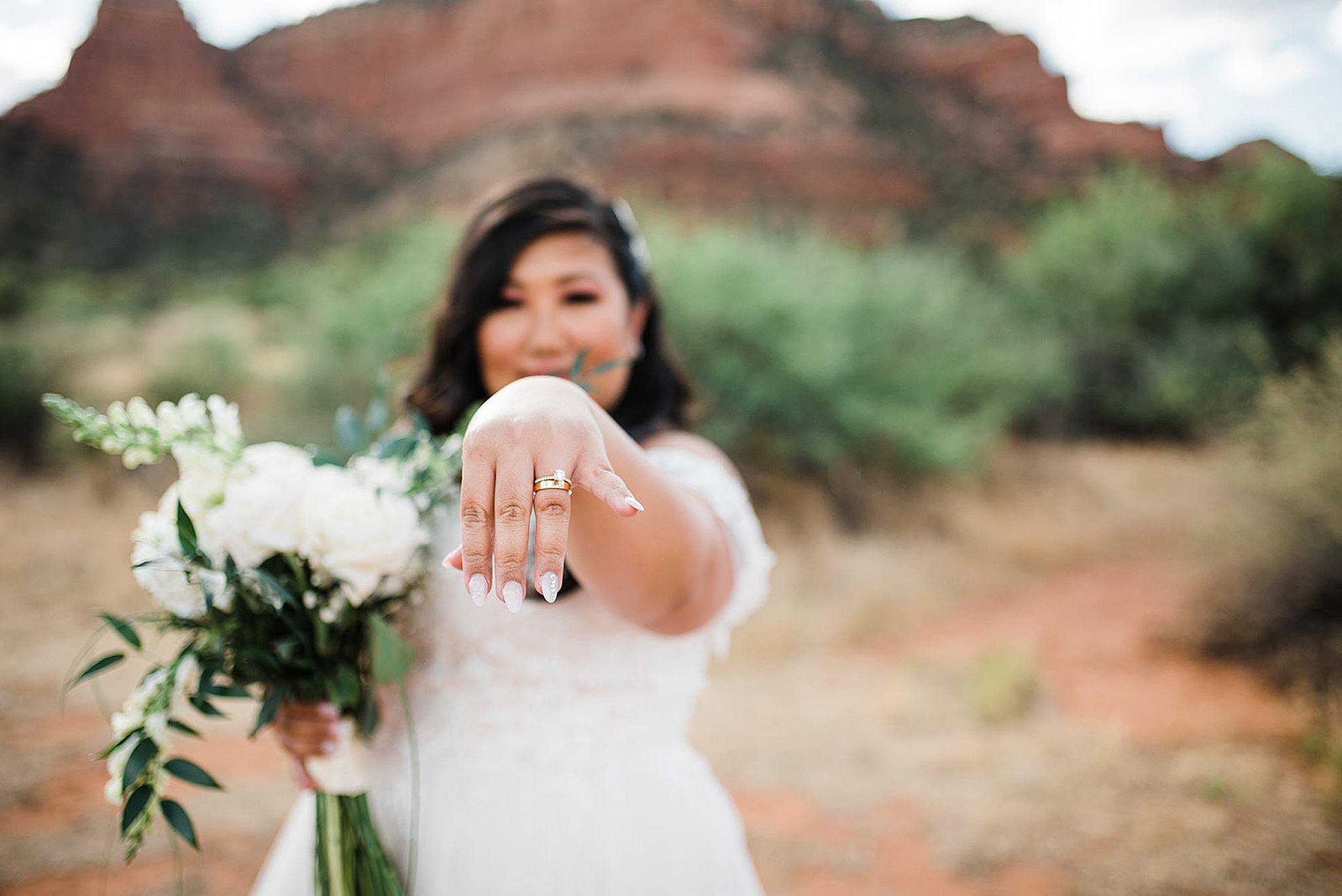bride stands in the desert with wedding rings and white bouquet sky ranch lodge wedding