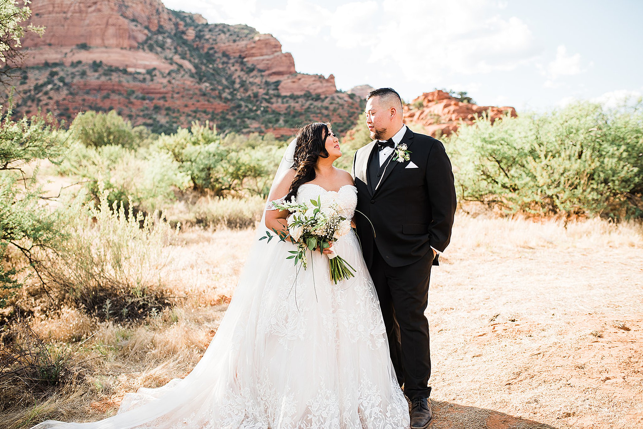 Bride and groom stand in the desert in front of red cliffs sky ranch lodge wedding