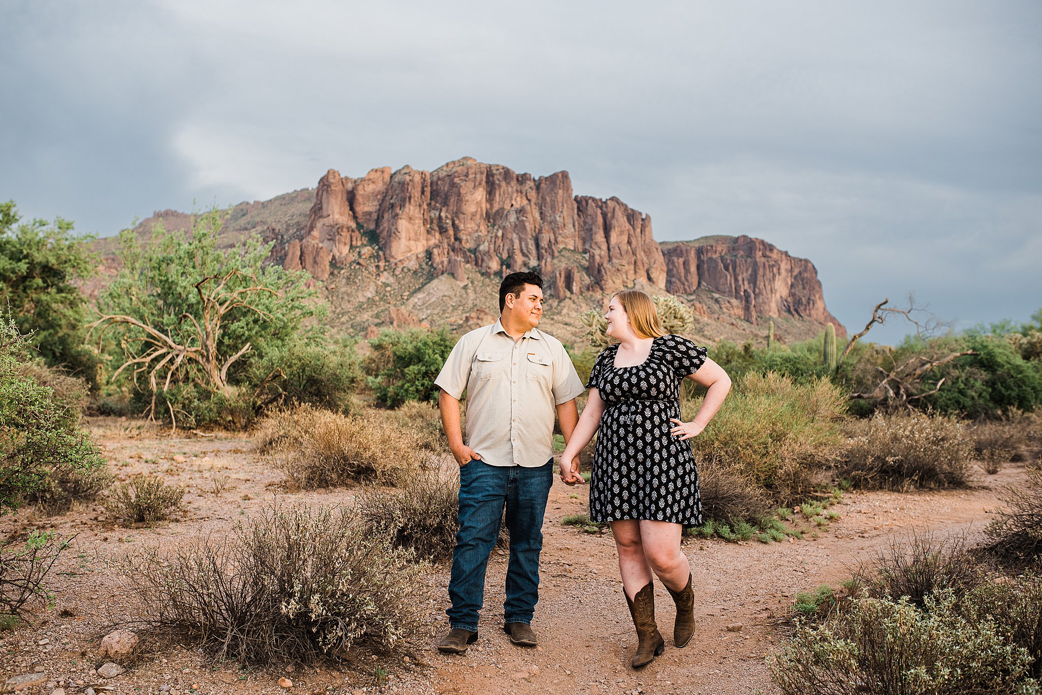 Couple holding hands and looking at each other stand in front of a mountain lost dutchman state park wedding