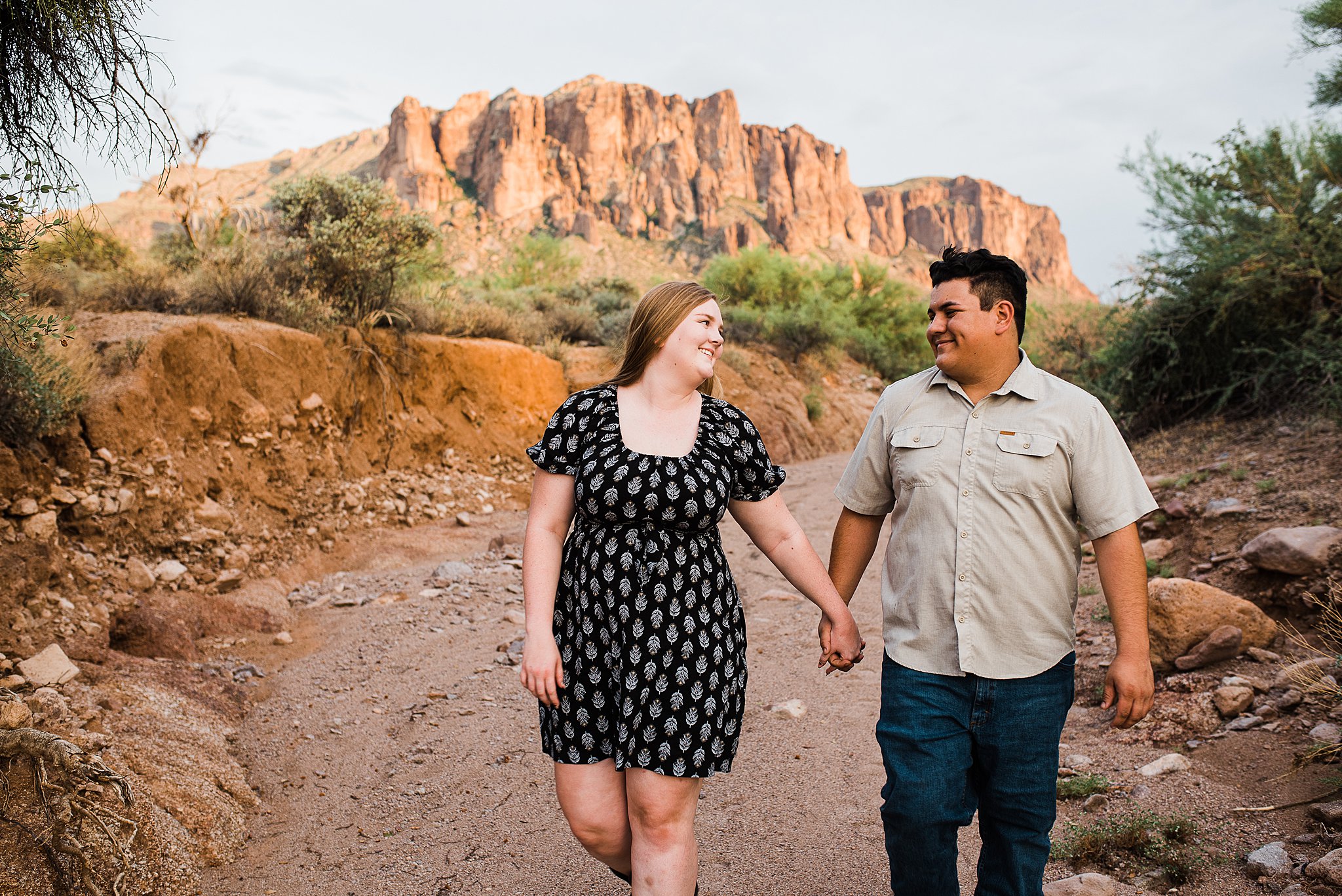 Engaged couple walk down a rocky desert path holding hands lost dutchman state park wedding