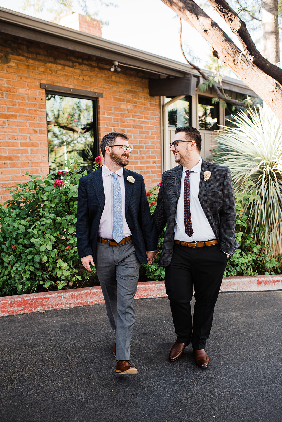 Newlywed men in suits with brown belts and shoes walk down the street in front of a brick building The Newton Phoenix