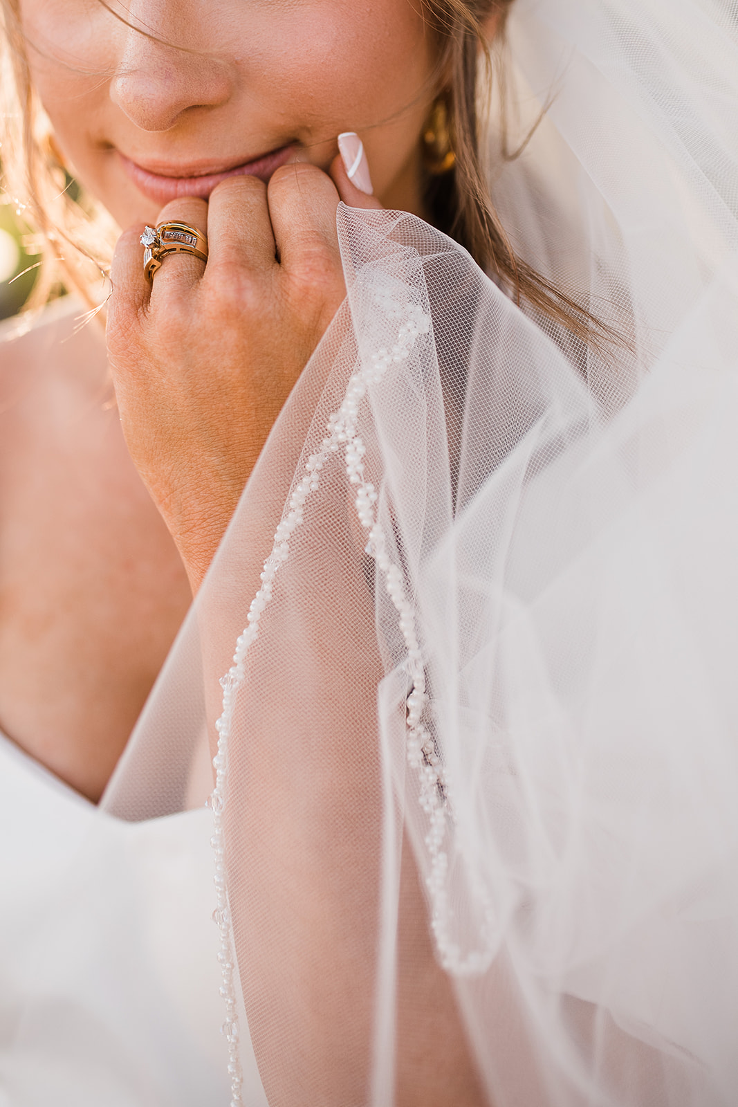 Details of a bride holding her veil up to her chin at sunset