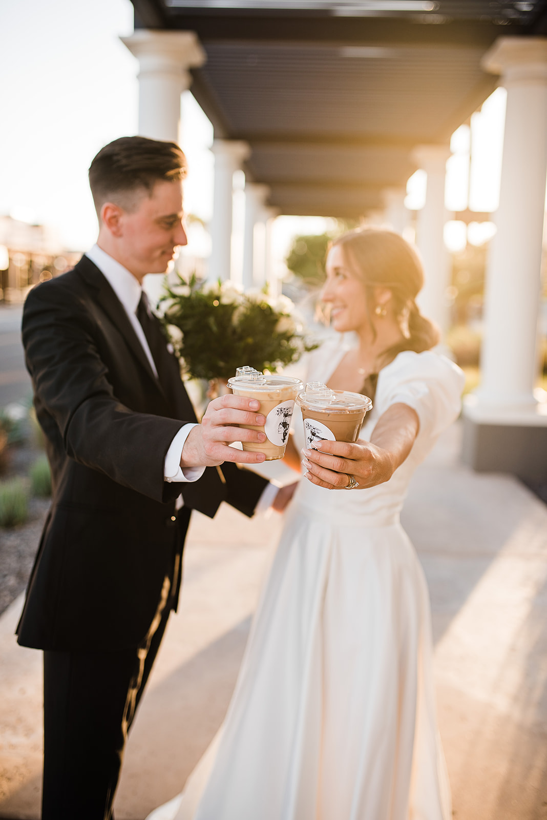 Newlyweds show off their coffee cups while standing under a covered walkway at sunset prepared by Phoenix Wedding Planners