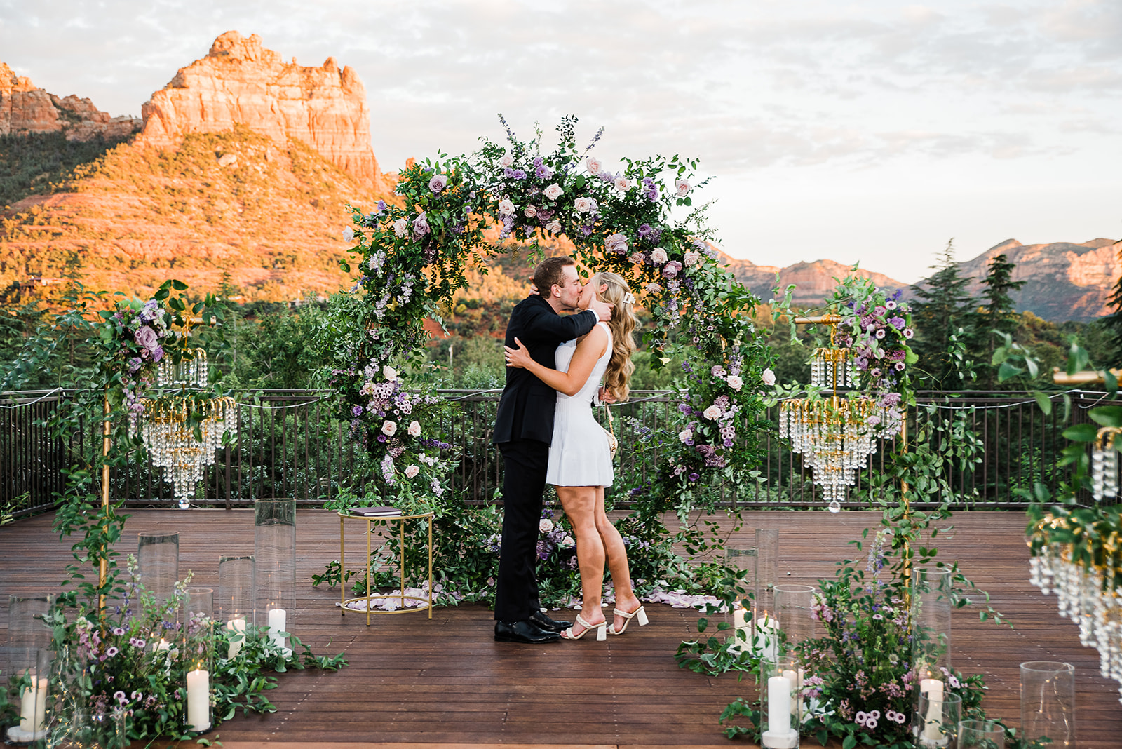 A newly engaged couple kisses while standing on a mountain overlook boardwalk in Sedona surrounded by romantic decorations