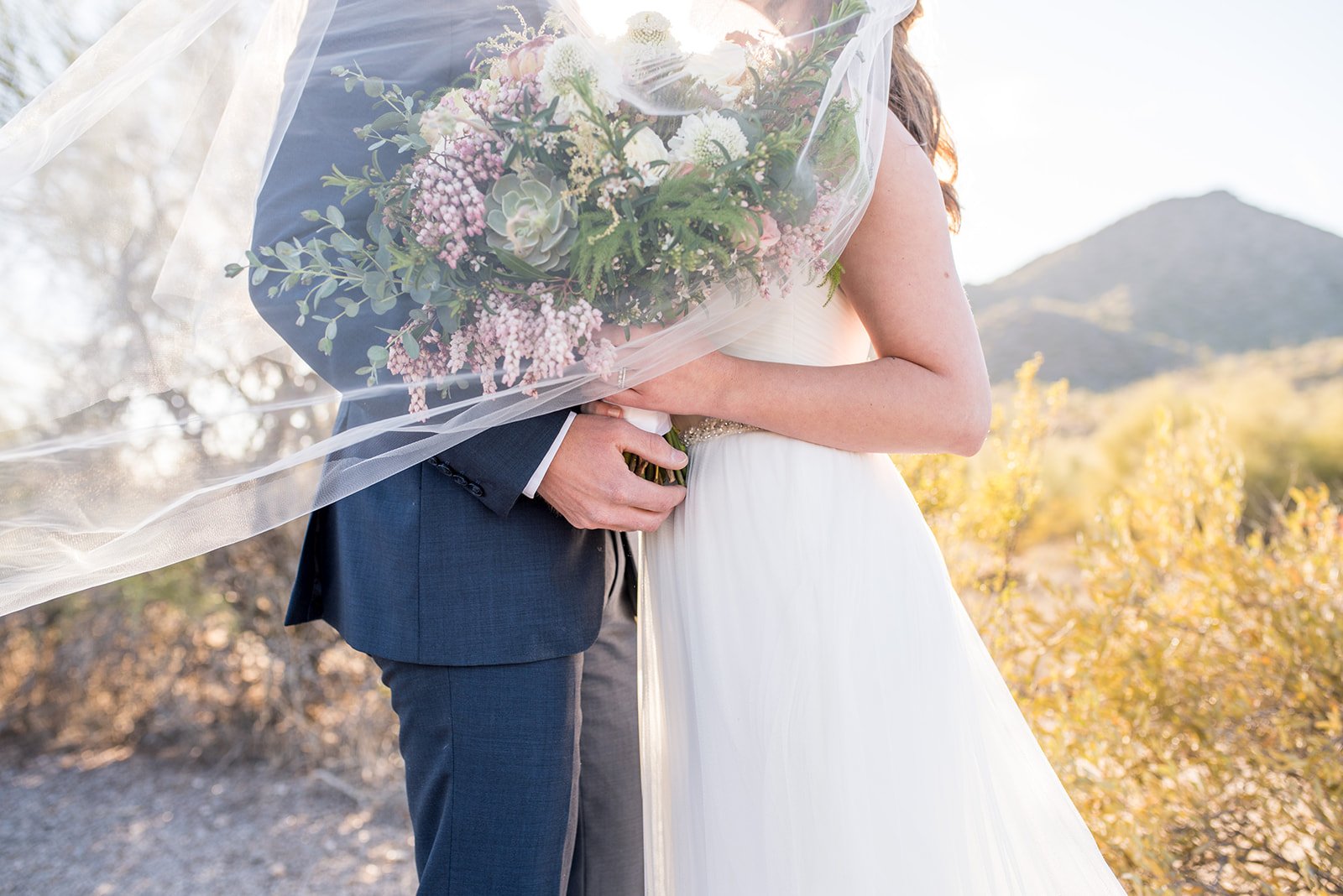 Details of newlyweds holding a large bouquet together while wrapped in a veil at a Country Club At DC Ranch