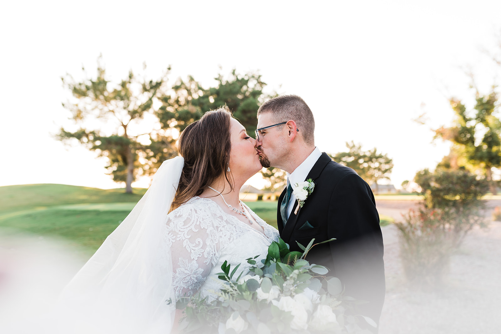 Newlyweds kiss in a garden at sunset while the veil flies around them at a Lindsay Grove Wedding