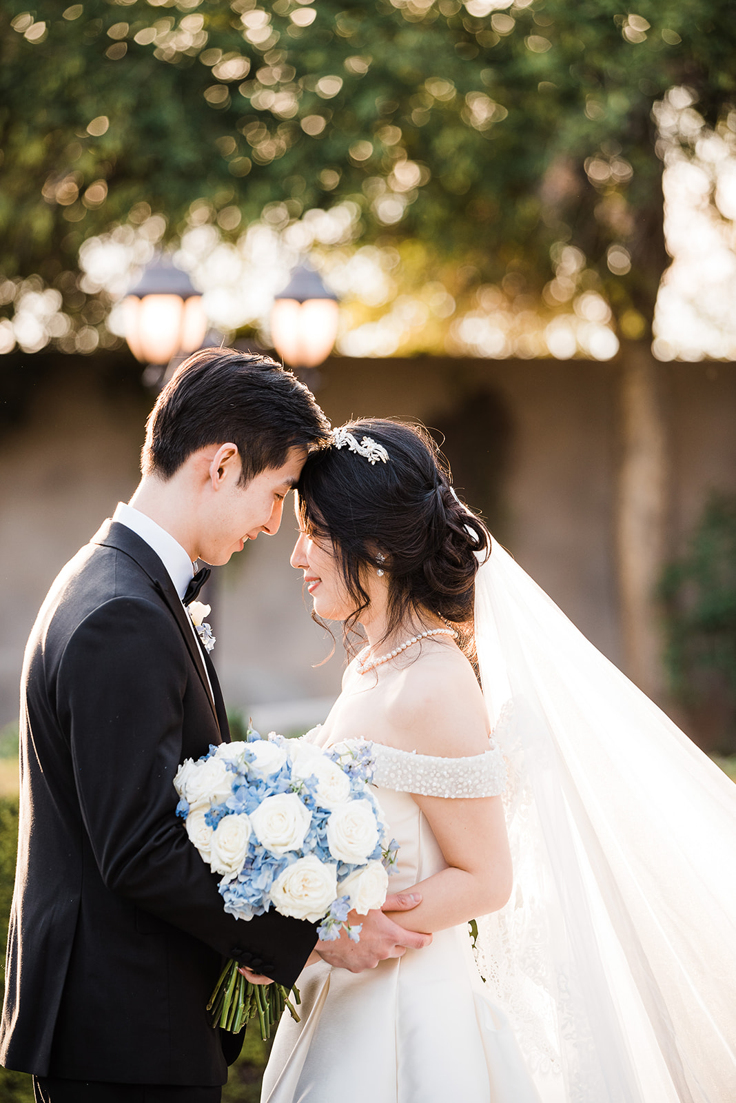 Newlyweds touch foreheads while standing in a garden at sunset