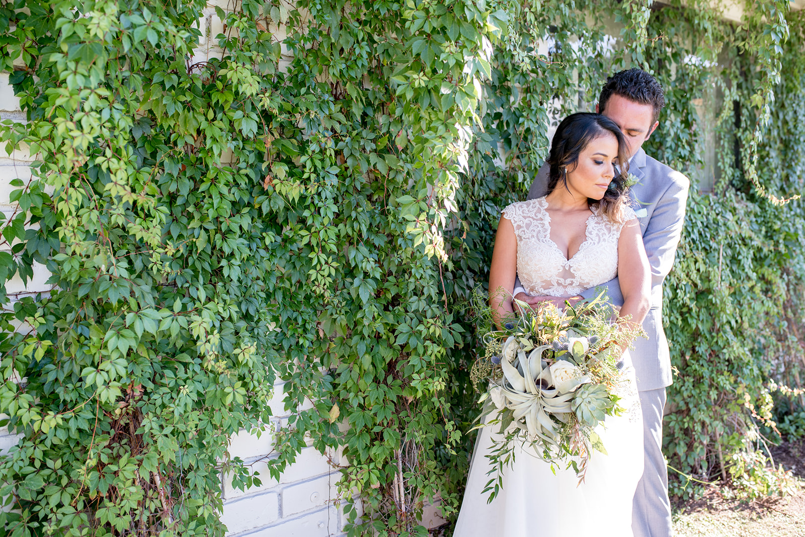 groom wraps his arms around his bride in front of a wall of ivy at a Villa Siena Wedding