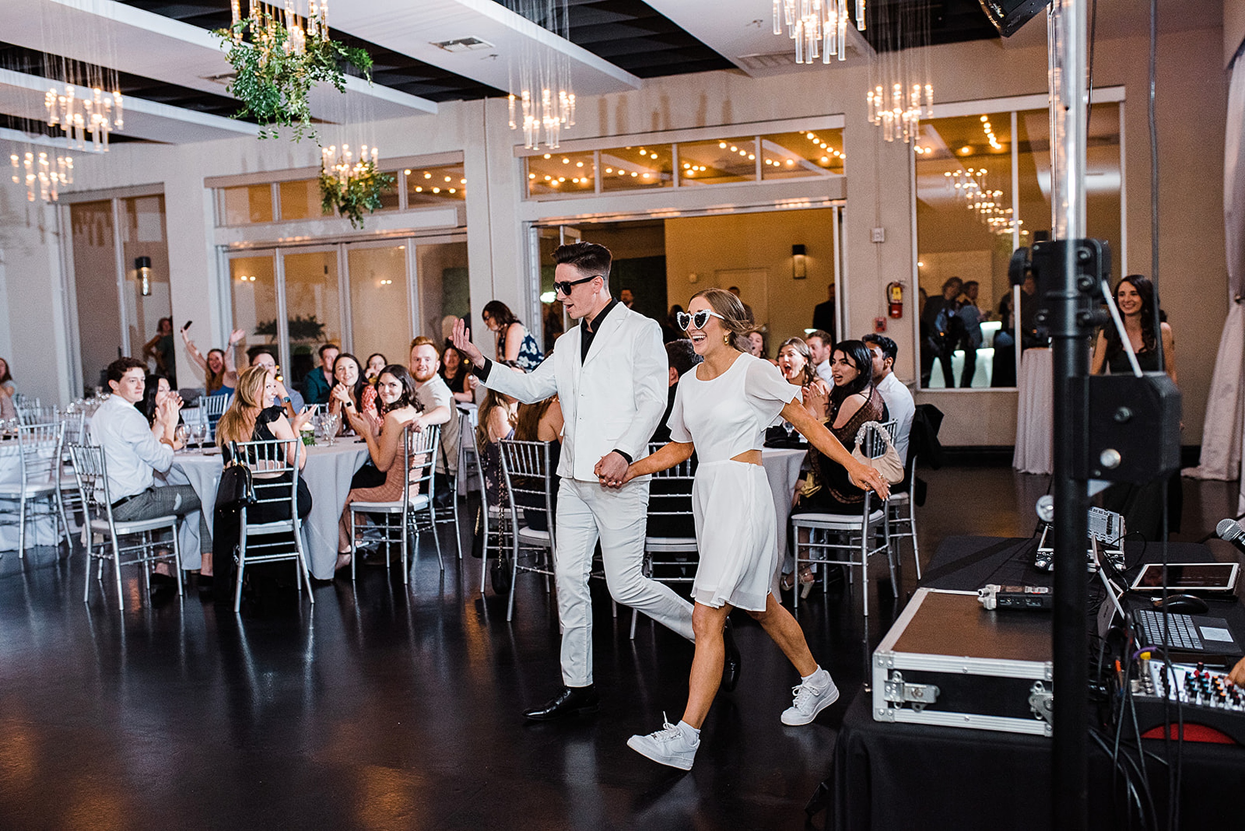 Newlyweds enter their reception both in white and sunglasses to cheers 