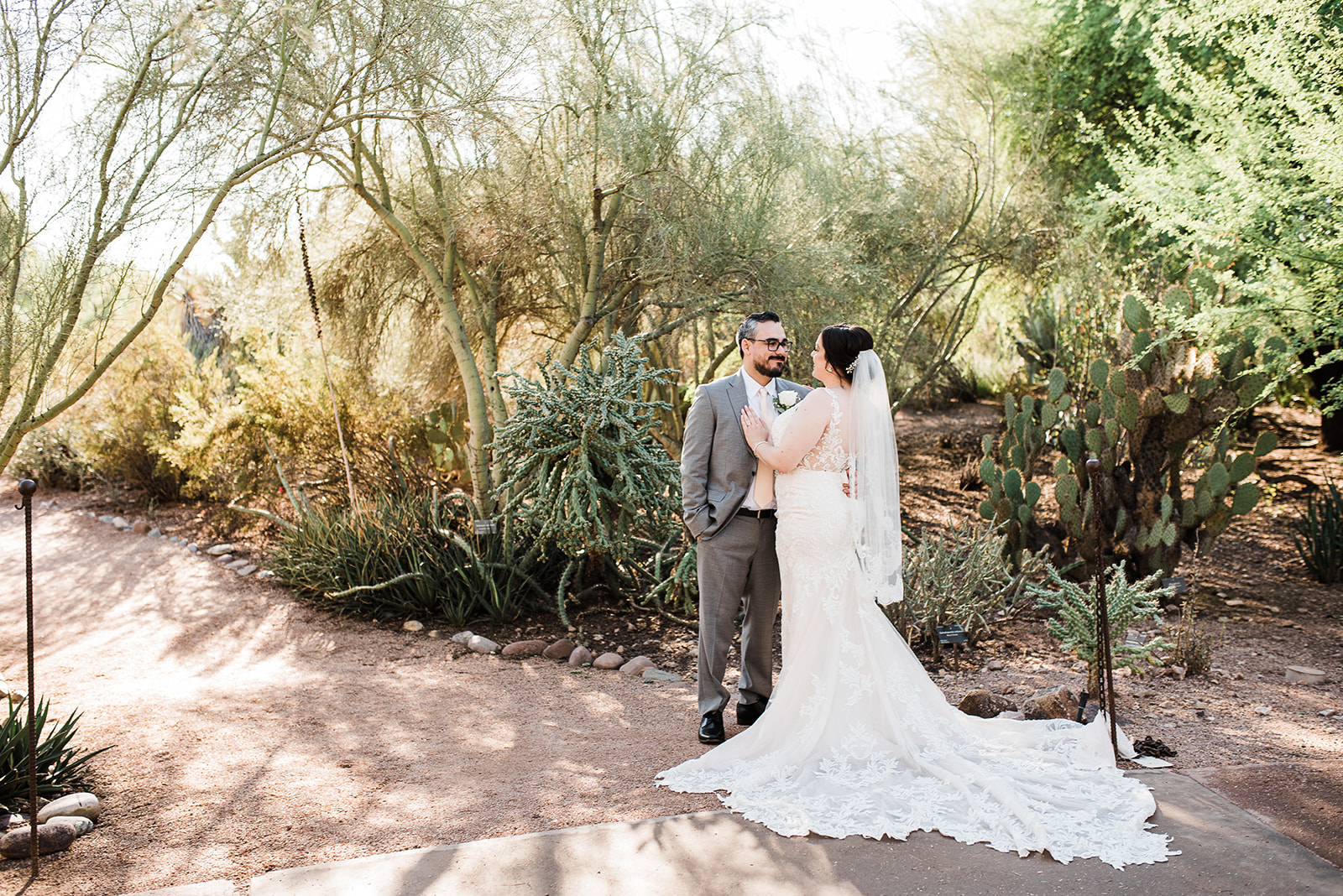Newlyweds stand in a desert garden at sunset with the bride's hand on the groom's chest at their The Phoenician Wedding